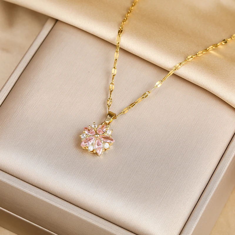 Pendentif fleur de cerisier en zircons roses posé sur un écrin beige, chaîne dorée à maillons plats.