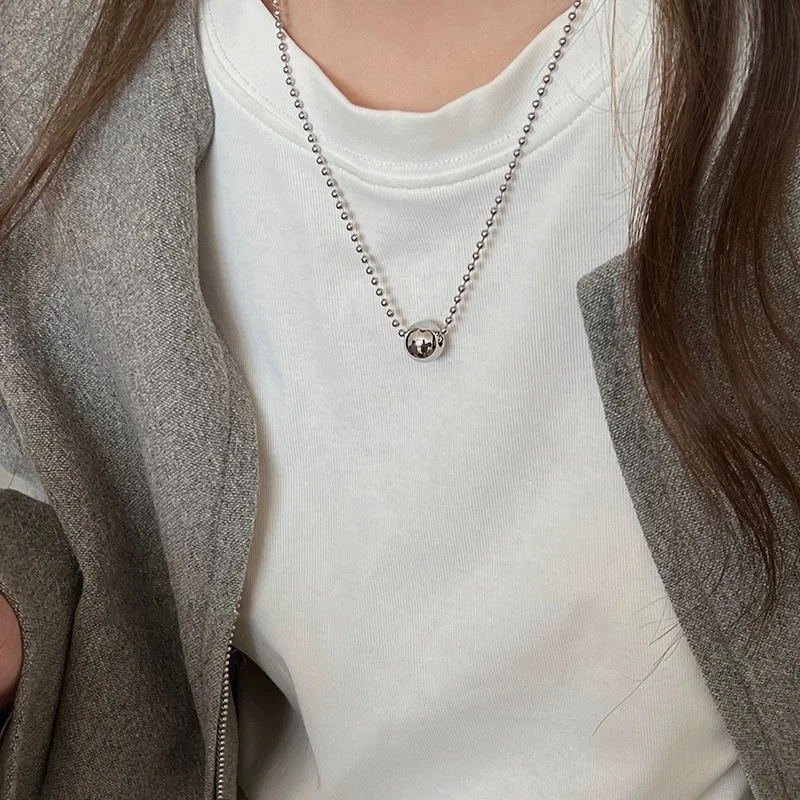Le collier à pendentif bille porté sur un tee-shirt blanc, la sphère centrée sous la clavicule.