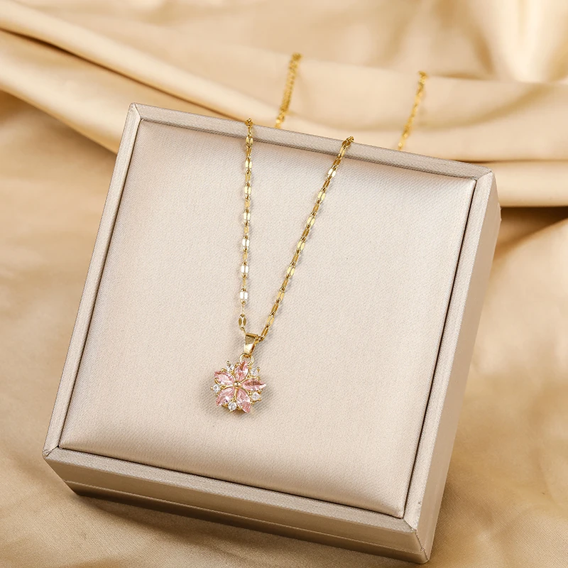 Le collier à pendentif fleur de cerisier présenté dans son écrin, chaîne dorée déployée en boucle.