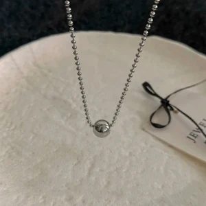 Collier à pendentif bille posé à plat sur une coupelle claire, chaîne à billes en acier argenté.