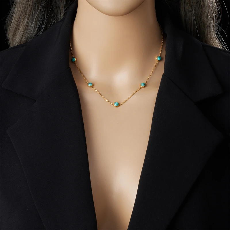 Le collier porté sur un buste, sous une veste noire ouverte : les cabochons turquoise se répartissent sous la clavicule