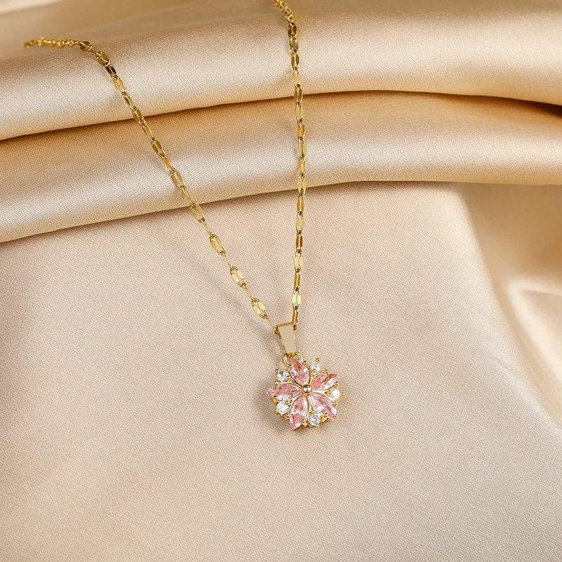 Le collier à pendentif fleur de cerisier posé à plat sur un drapé de satin ivoire.