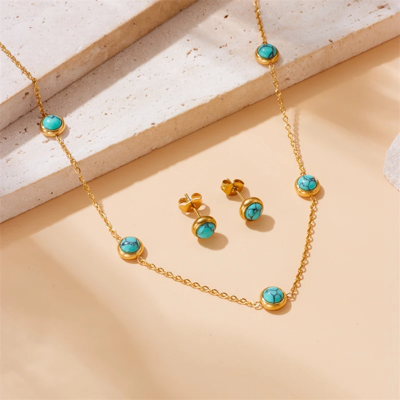 Le collier et les puces d'oreilles photographiés sur un fond sable, près d'une pierre claire, en lumière rasante