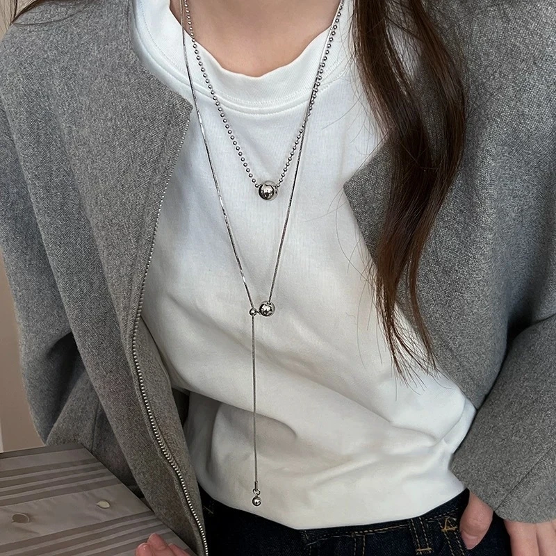 Les deux colliers portés en superposition sur un tee-shirt blanc, chaîne à billes et sautoir fin.