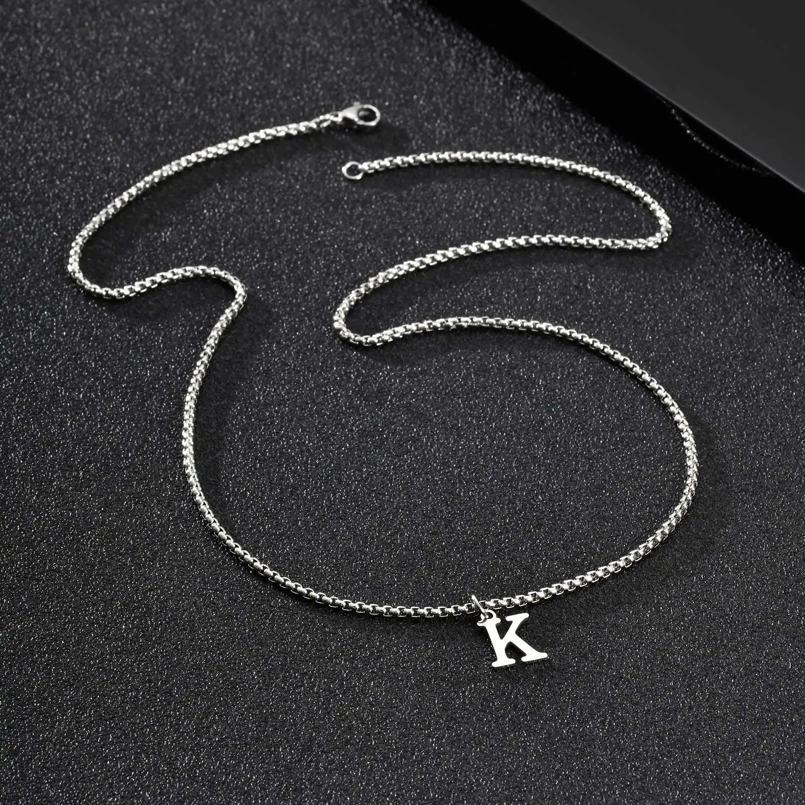 Le collier entier posé à plat, chaîne maille boîte et fermoir à ressort visibles, avec son pendentif lettre K